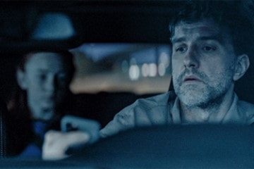 Mann som ser på mobilen mens han kjører bil med barn i baksetet